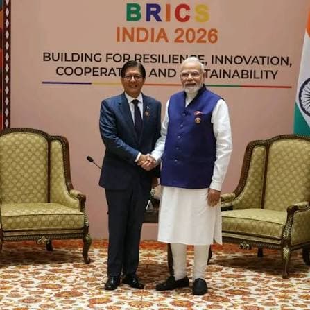 एक व्यक्ति सफेद शर्ट पहने हुए मुस्कुरा रहा है, जिसके पीछे एक लकड़ी की दीवार है।